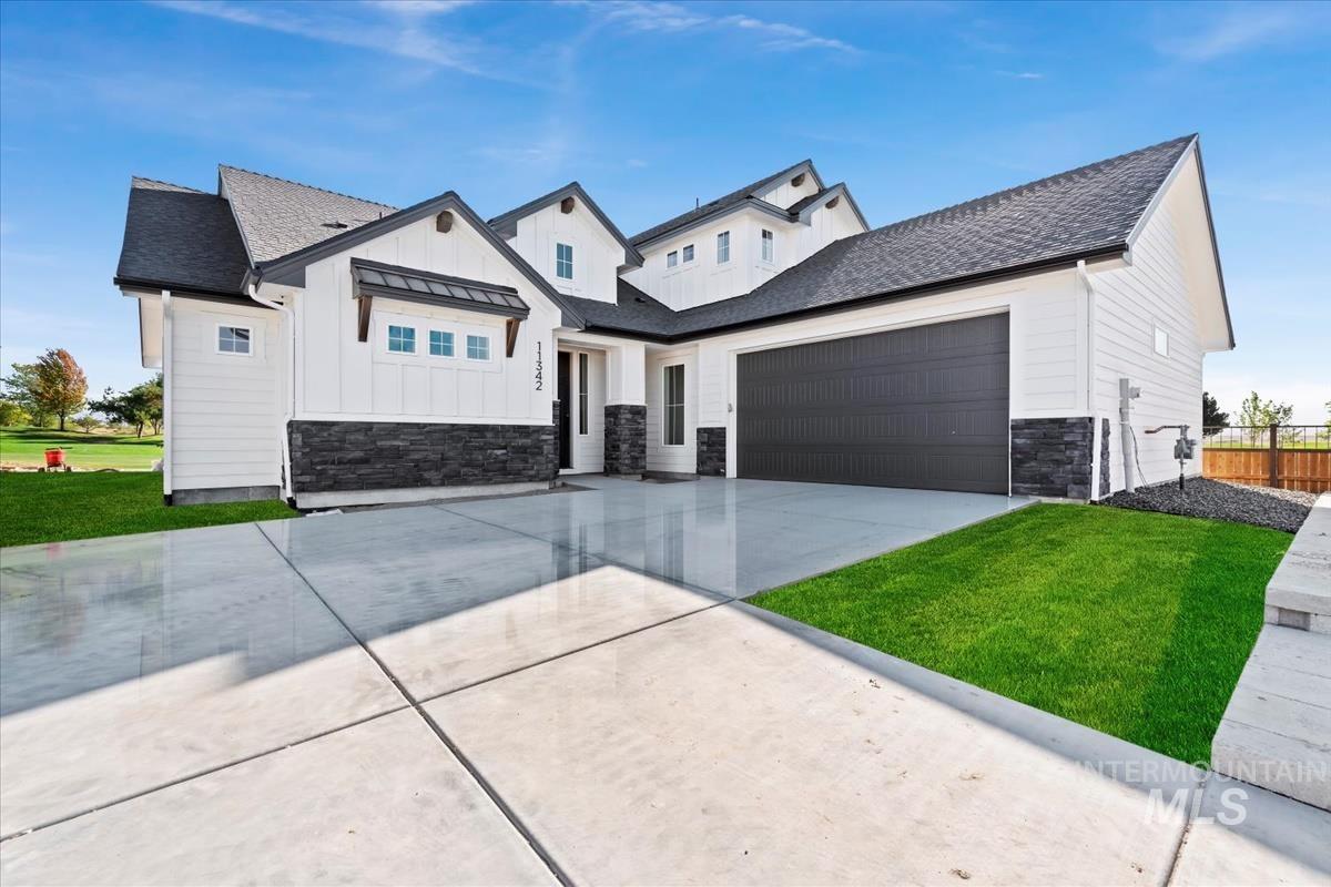 Modern farmhouse exterior featuring white board and batten siding, dark stone accents, and a contrasting dark gray garage door