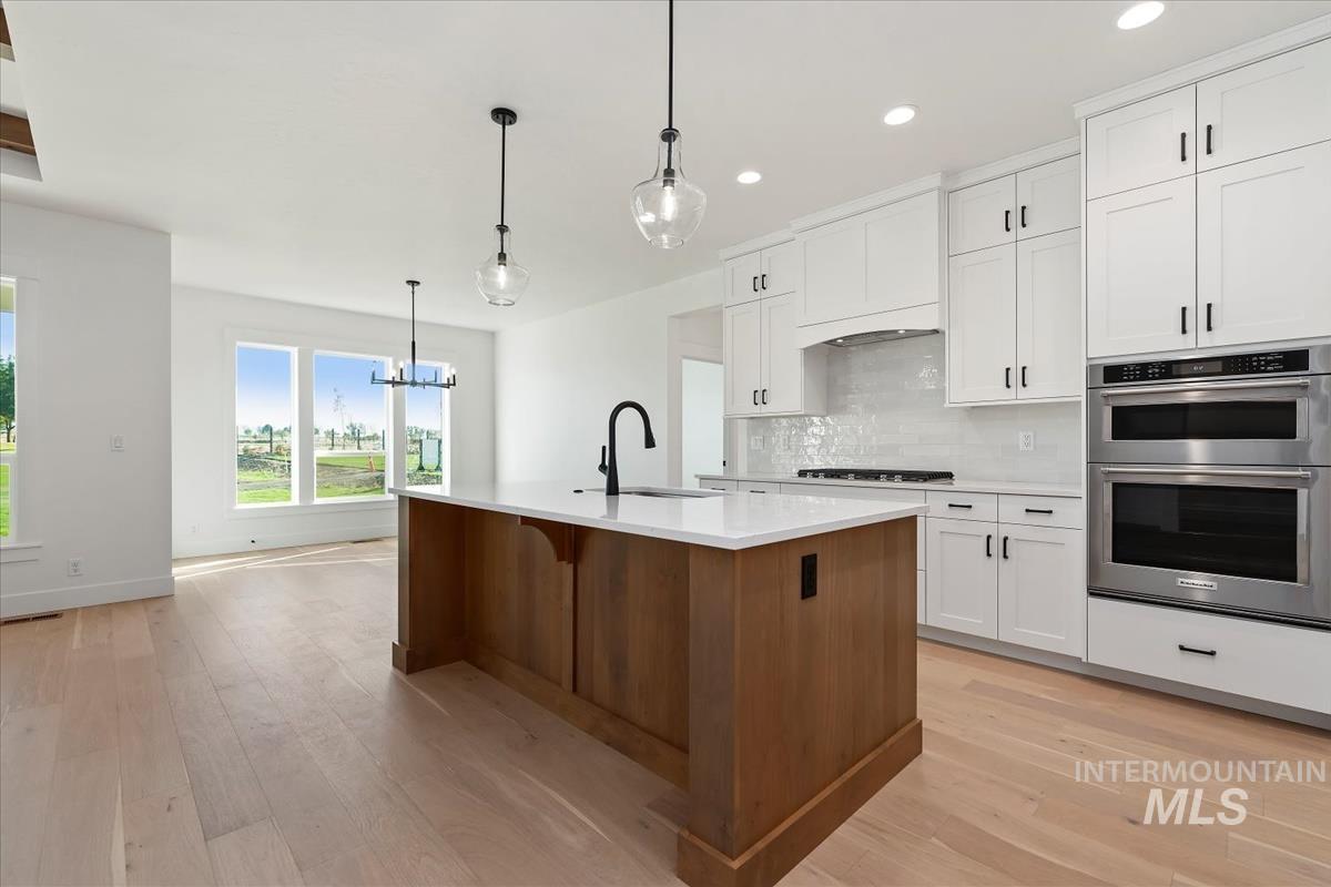 Open-concept kitchen featuring a wood-finish island with a white countertop, white cabinetry with matte black hardware, stainless steel appliances, and wood-finish flooring