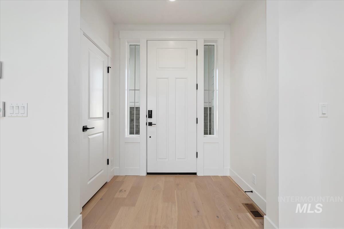 Entryway featuring a paneled door with sidelights, light wood-finish flooring, and white trim