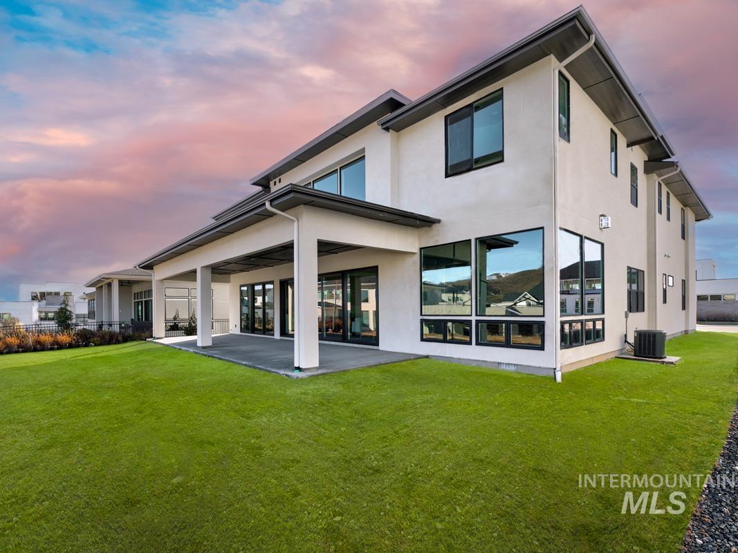 Back of property at dusk featuring stucco siding, a lawn, and a patio