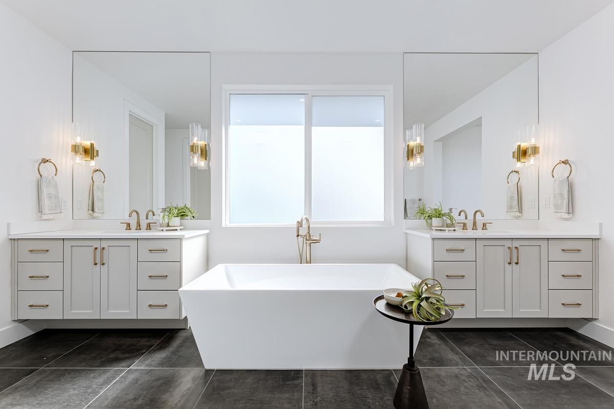 Full bath with two vanities, a freestanding tub, and dark tile patterned flooring