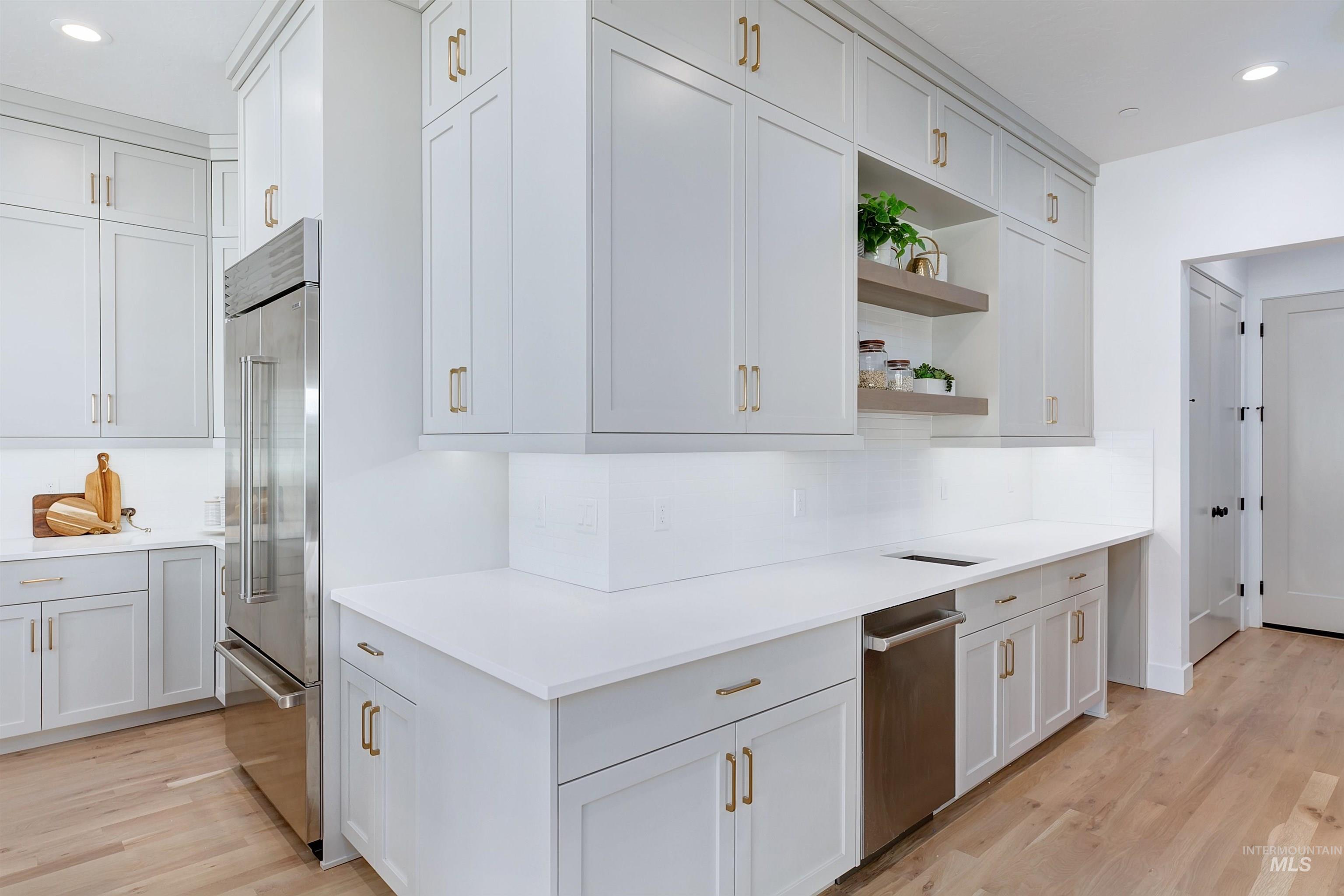 Kitchen with recessed lighting, open shelves, light wood-type flooring, appliances with stainless steel finishes, and white cabinets