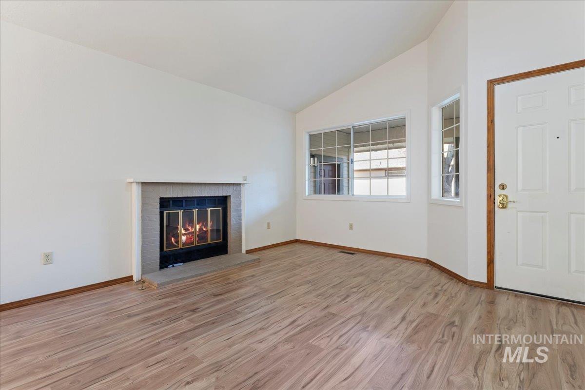 Unfurnished living room featuring lofted ceiling, light wood-type flooring, and a brick fireplace