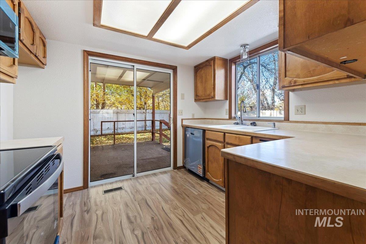 Kitchen with light countertops, brown cabinets, light wood-style flooring, appliances with stainless steel finishes, and plenty of natural light
