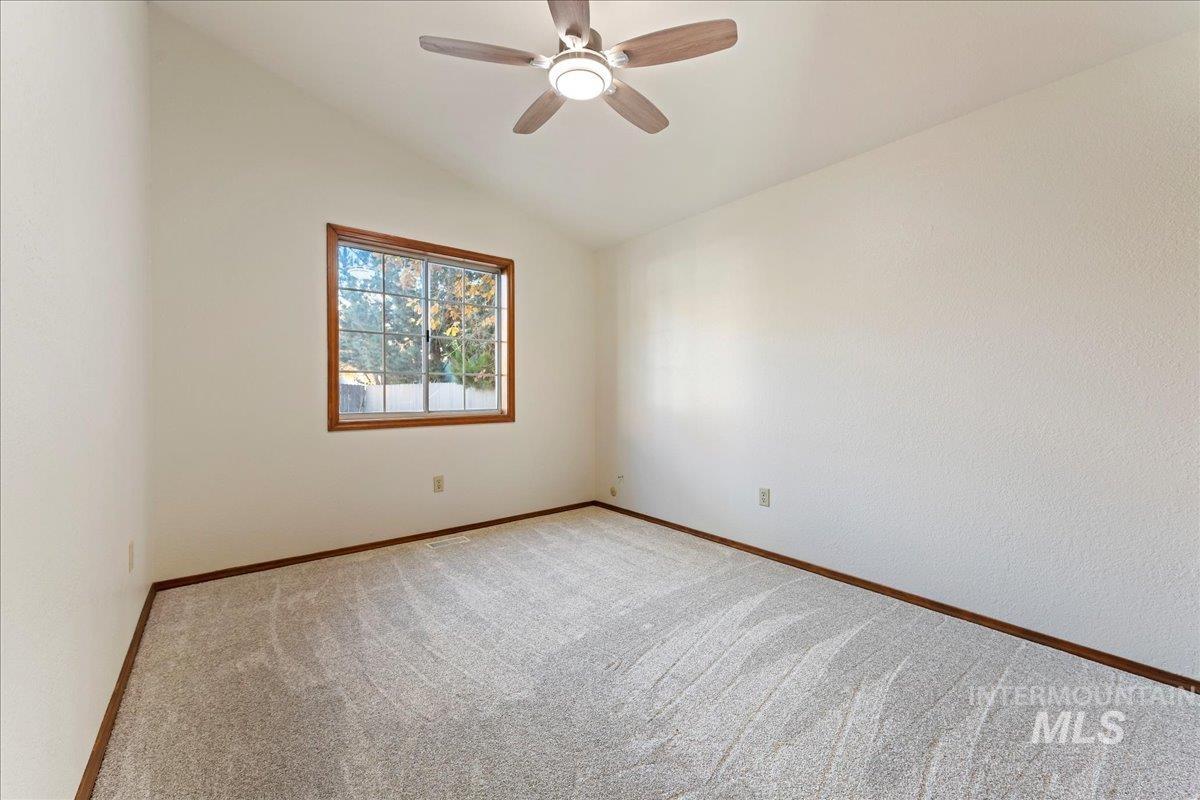 Carpeted empty room featuring vaulted ceiling and a ceiling fan