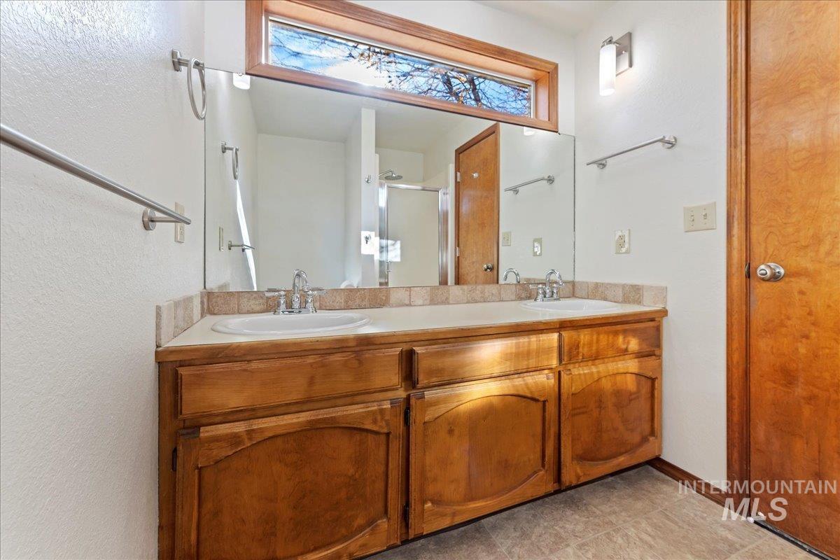 Bathroom featuring double vanity, a shower stall, a textured wall, and light tile patterned floors