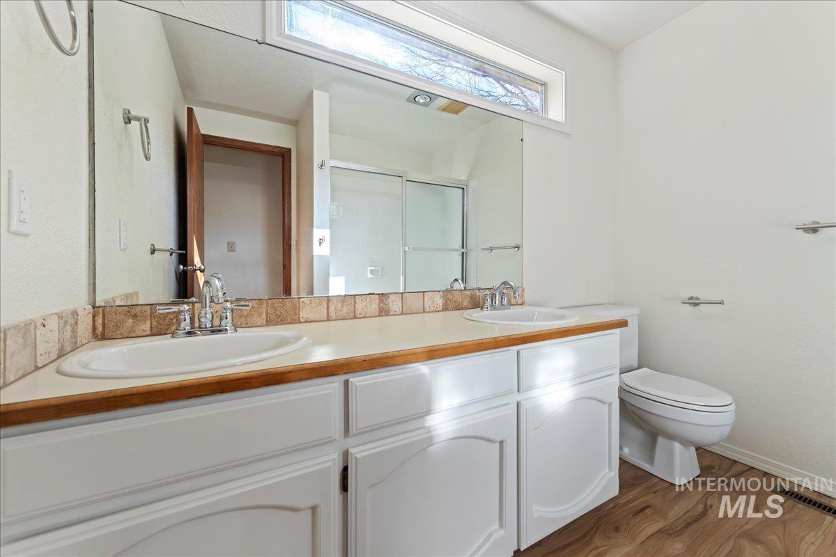 Full bathroom with double vanity, a stall shower, and dark wood-style floors