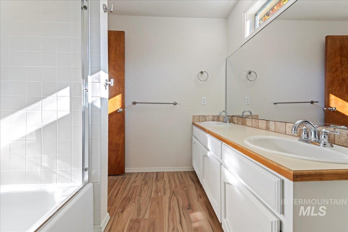 Bathroom with double vanity, light wood-style flooring, shower / bath combination with glass door, and a textured wall