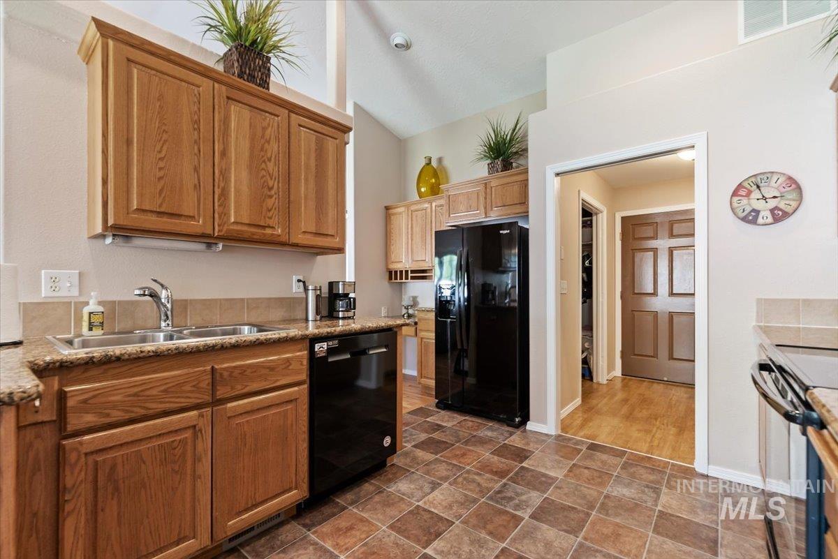 Kitchen with black appliances, stone finish flooring, lofted ceiling, and light stone countertops