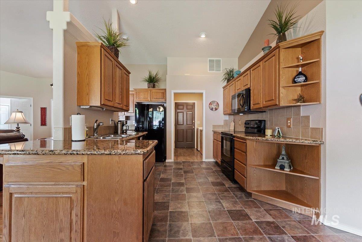 Kitchen featuring open shelves, dark stone countertops, black appliances, a peninsula, and wood finish cabinetry