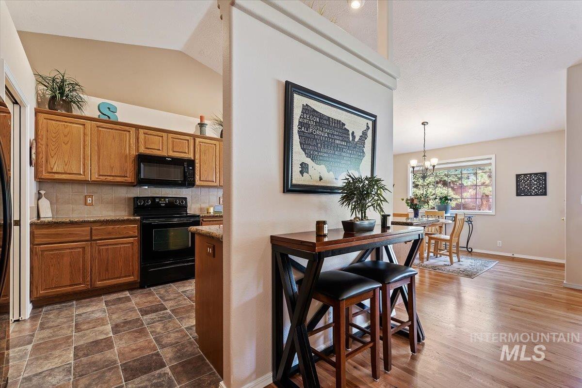 Kitchen featuring black appliances, tasteful backsplash, wood finish cabinets, light stone countertops, and hanging lights