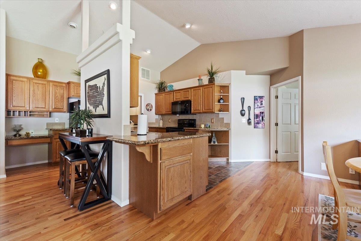 Kitchen with a kitchen breakfast bar, dark stone counters, wood finish cabinets, open shelves, and black appliances