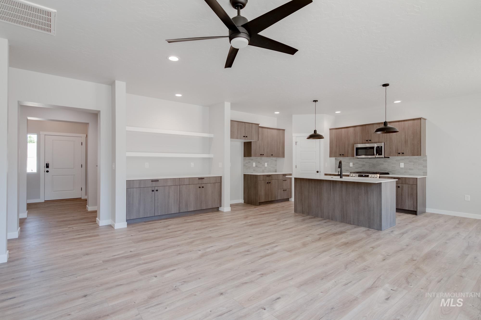 Kitchen featuring an island with sink, pendant lighting, open floor plan, light wood-type flooring, and recessed lighting