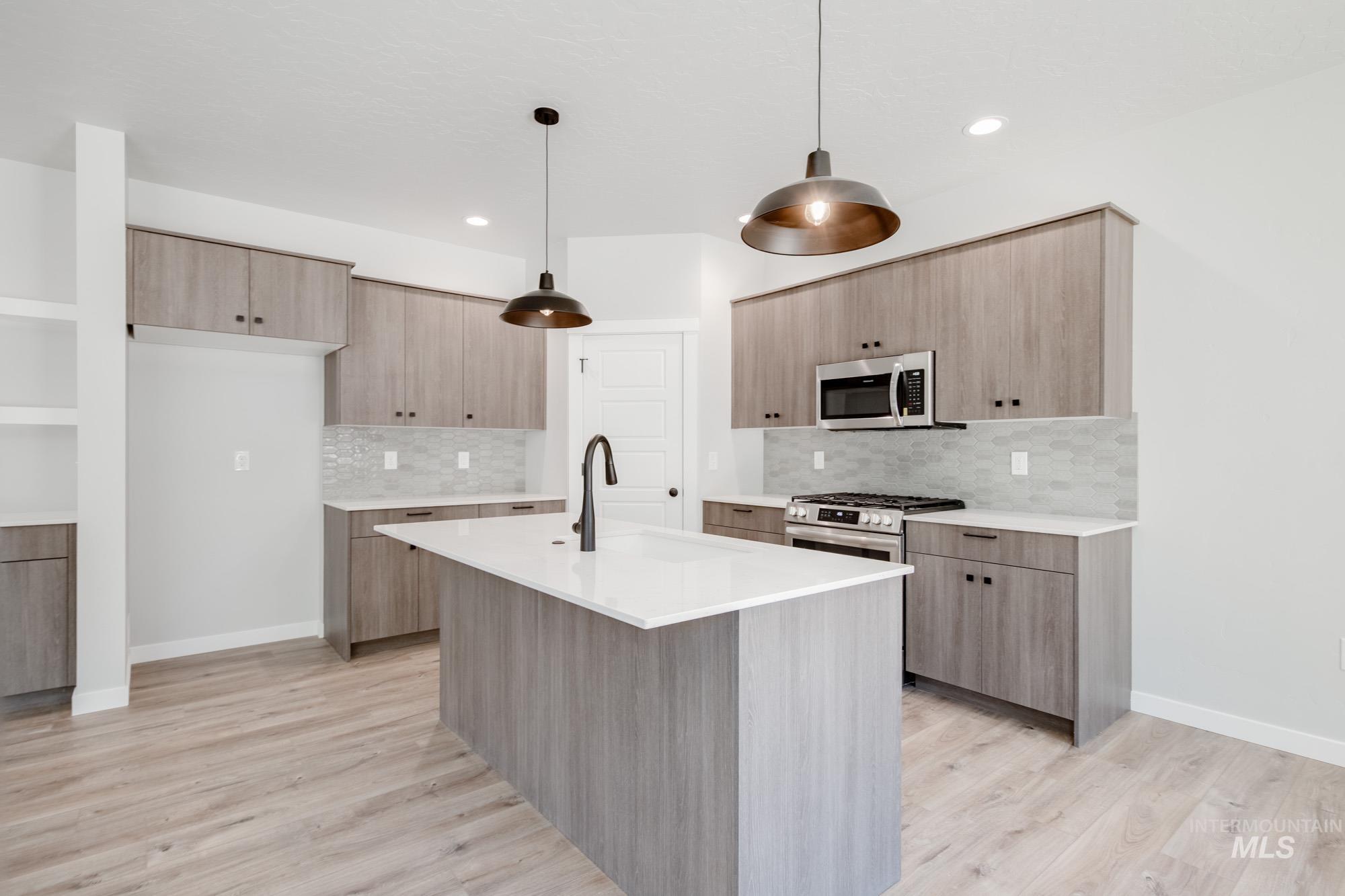 Kitchen featuring pendant lighting, light stone counters, light wood-style flooring, modern cabinets, and an island with sink