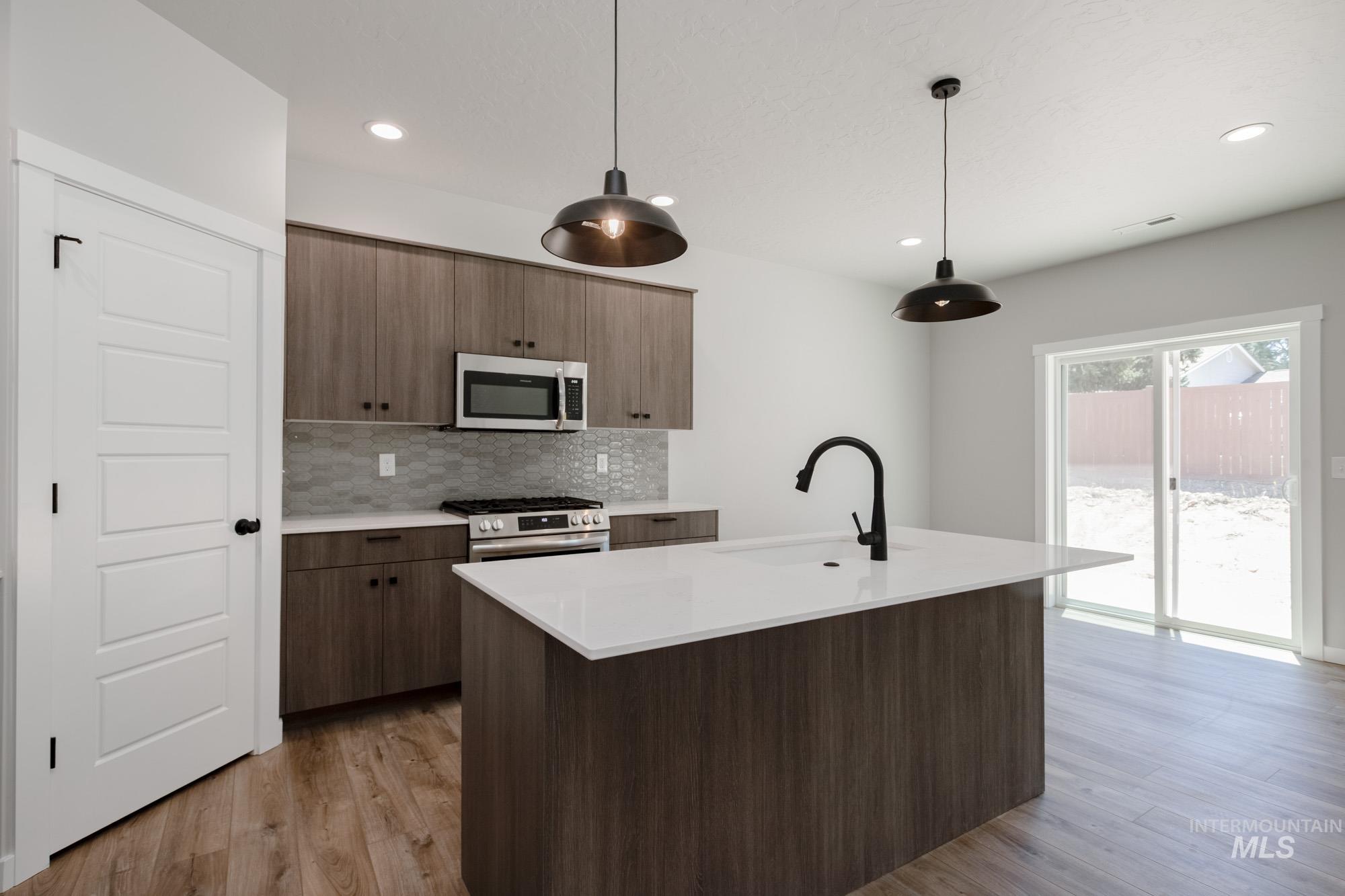 Kitchen featuring backsplash, pendant lighting, stainless steel appliances, light wood-style flooring, and a center island with sink