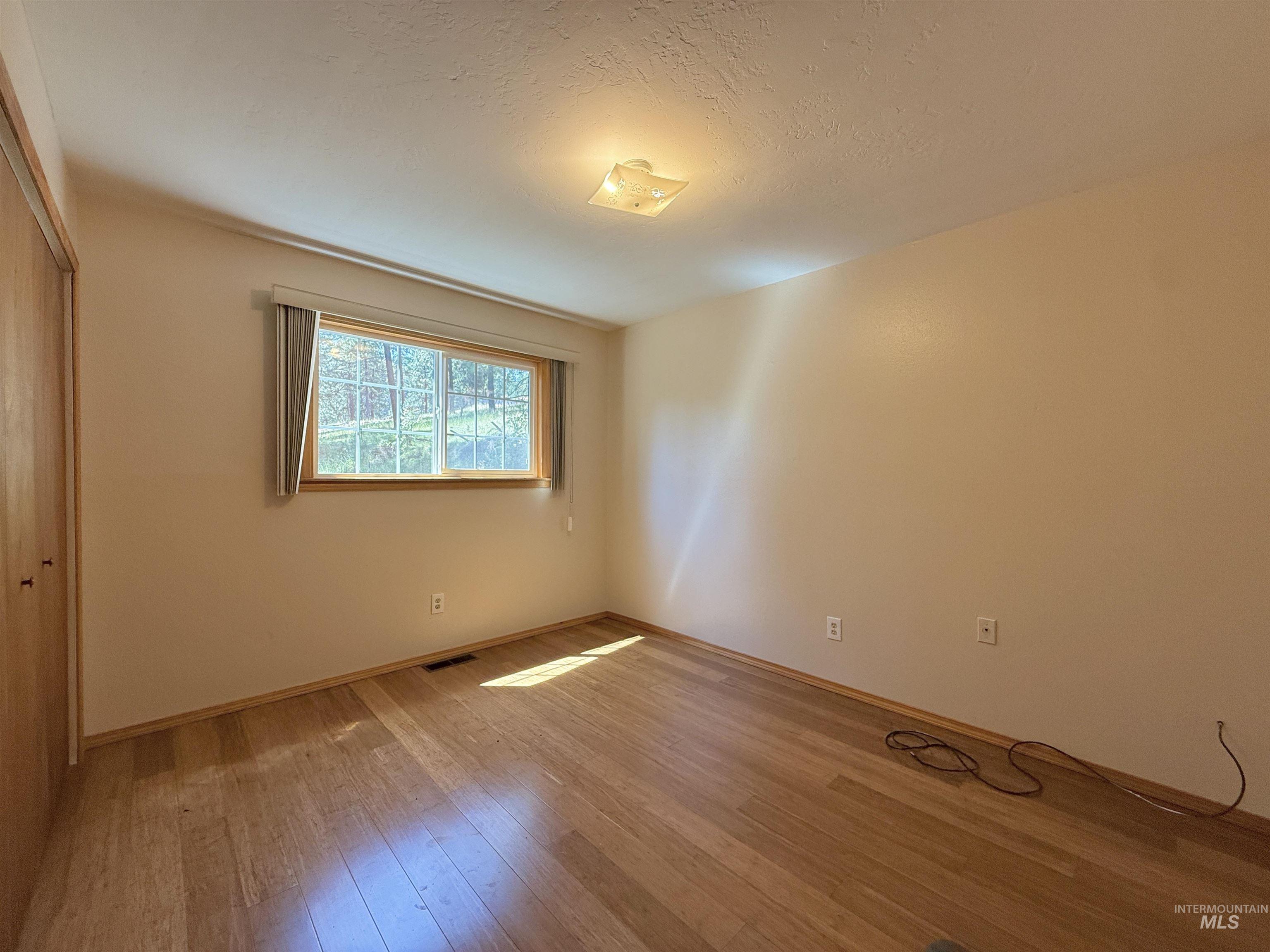 Unfurnished bedroom with light wood-style floors, a textured ceiling, and a closet