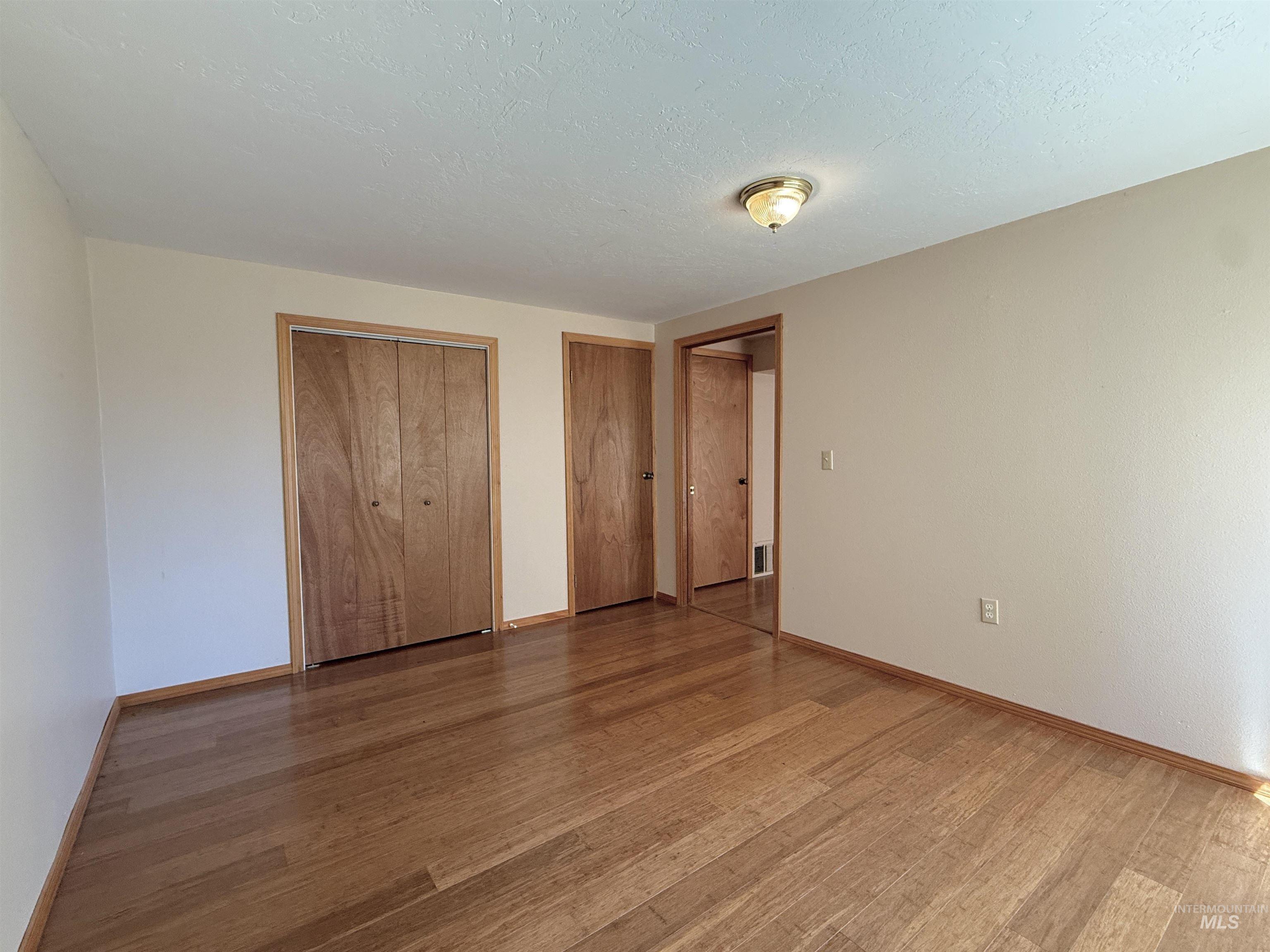 Unfurnished bedroom featuring two closets, light wood-style flooring, and a textured ceiling