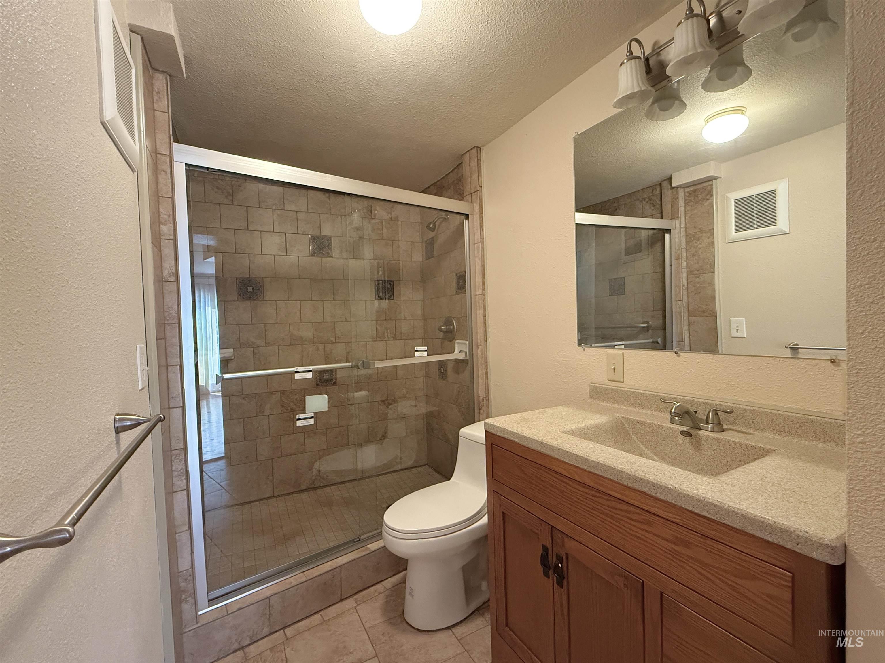 Bathroom with a textured wall, a textured ceiling, vanity, a shower stall, and tile patterned floors