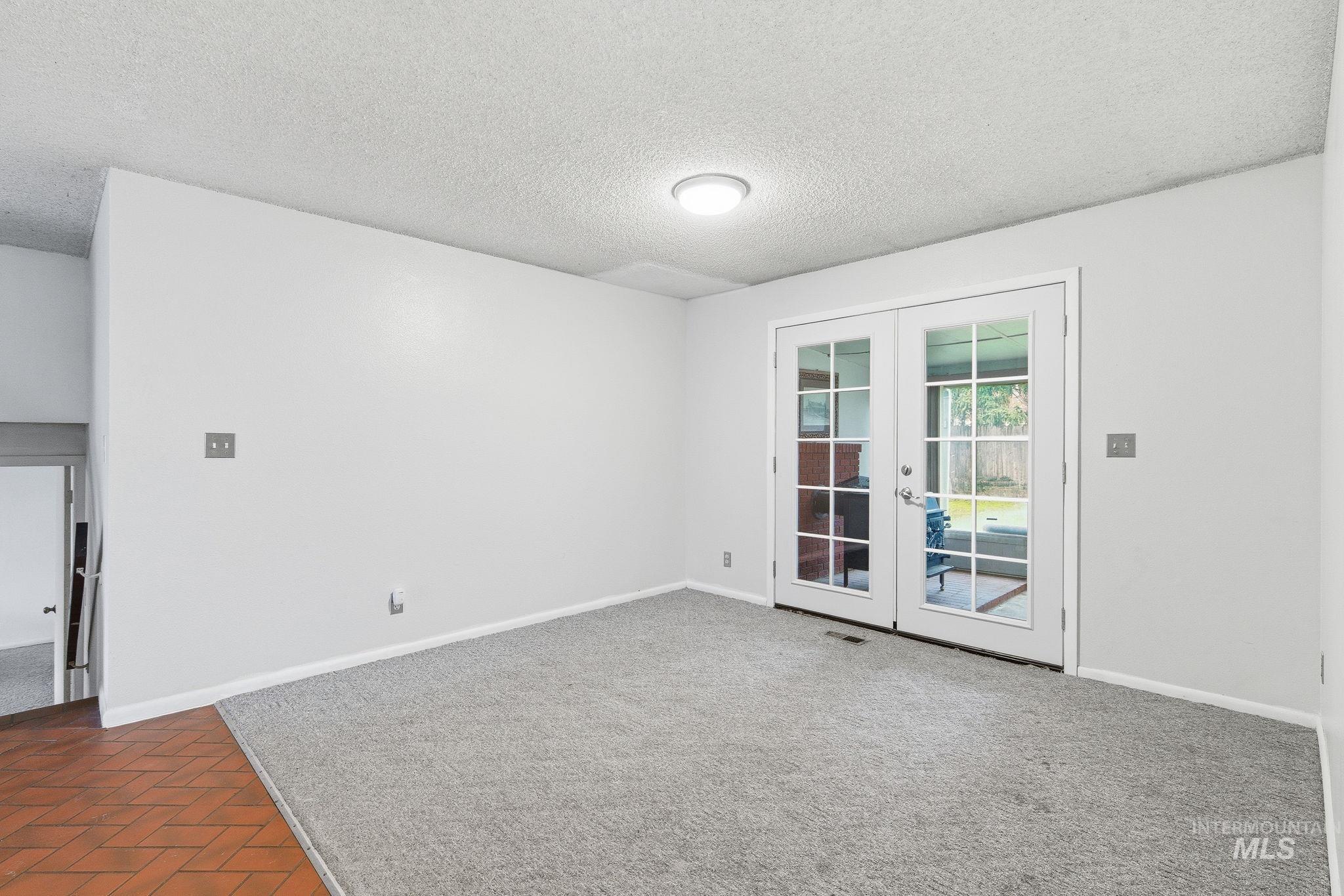 Unfurnished room featuring a textured ceiling, french doors, and dark carpet