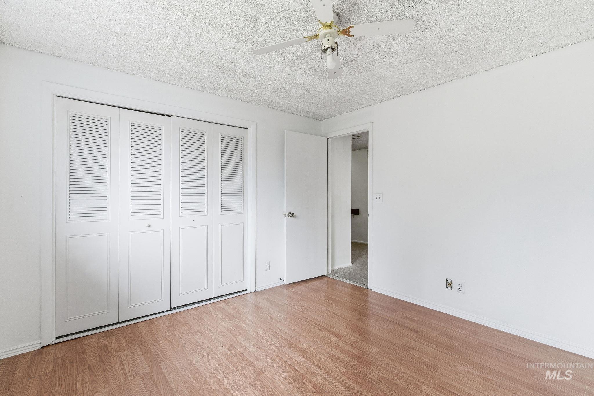 Unfurnished bedroom with a textured ceiling, a closet, ceiling fan, and wood finished floors