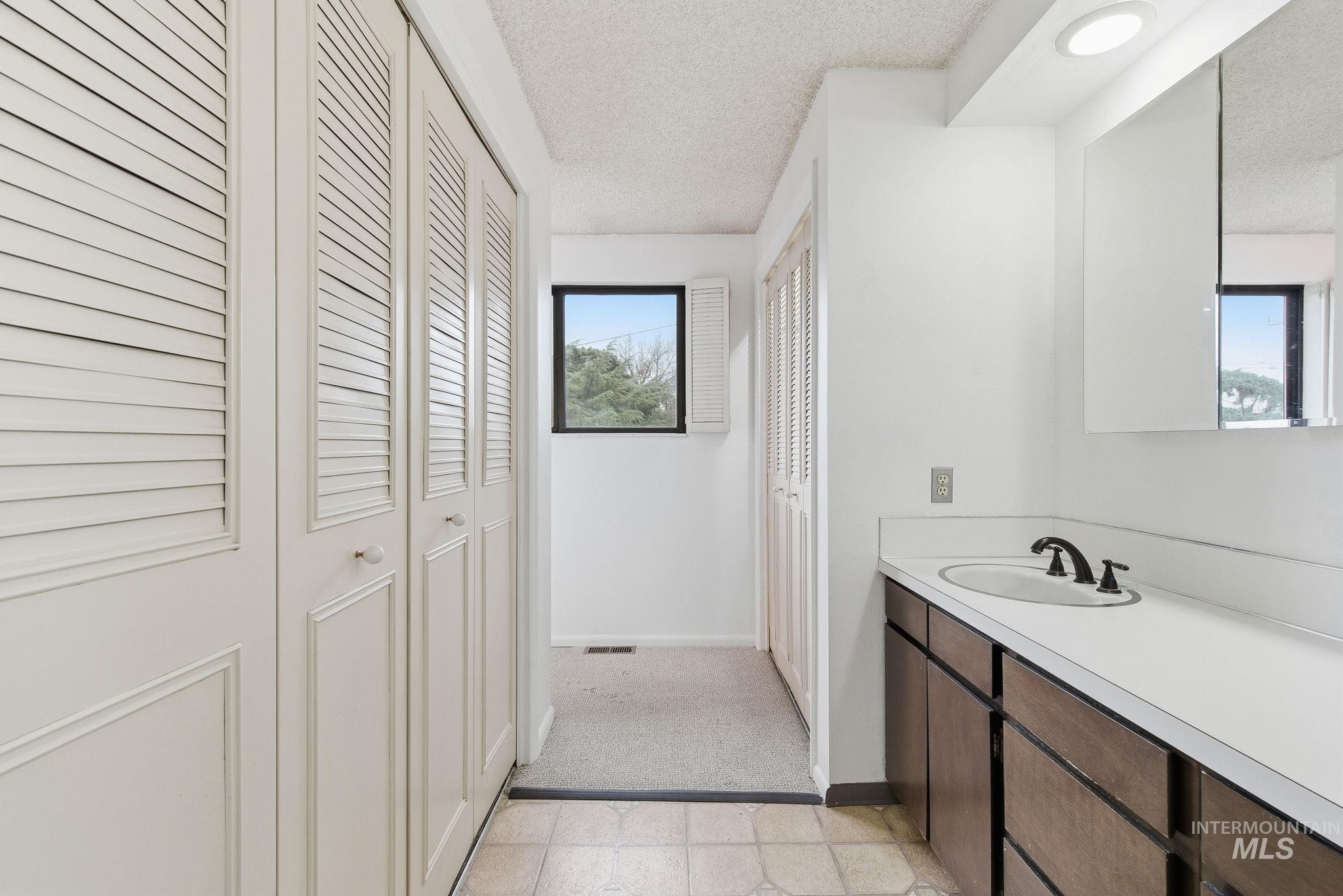Bathroom featuring a closet, a textured ceiling, vanity, and light flooring