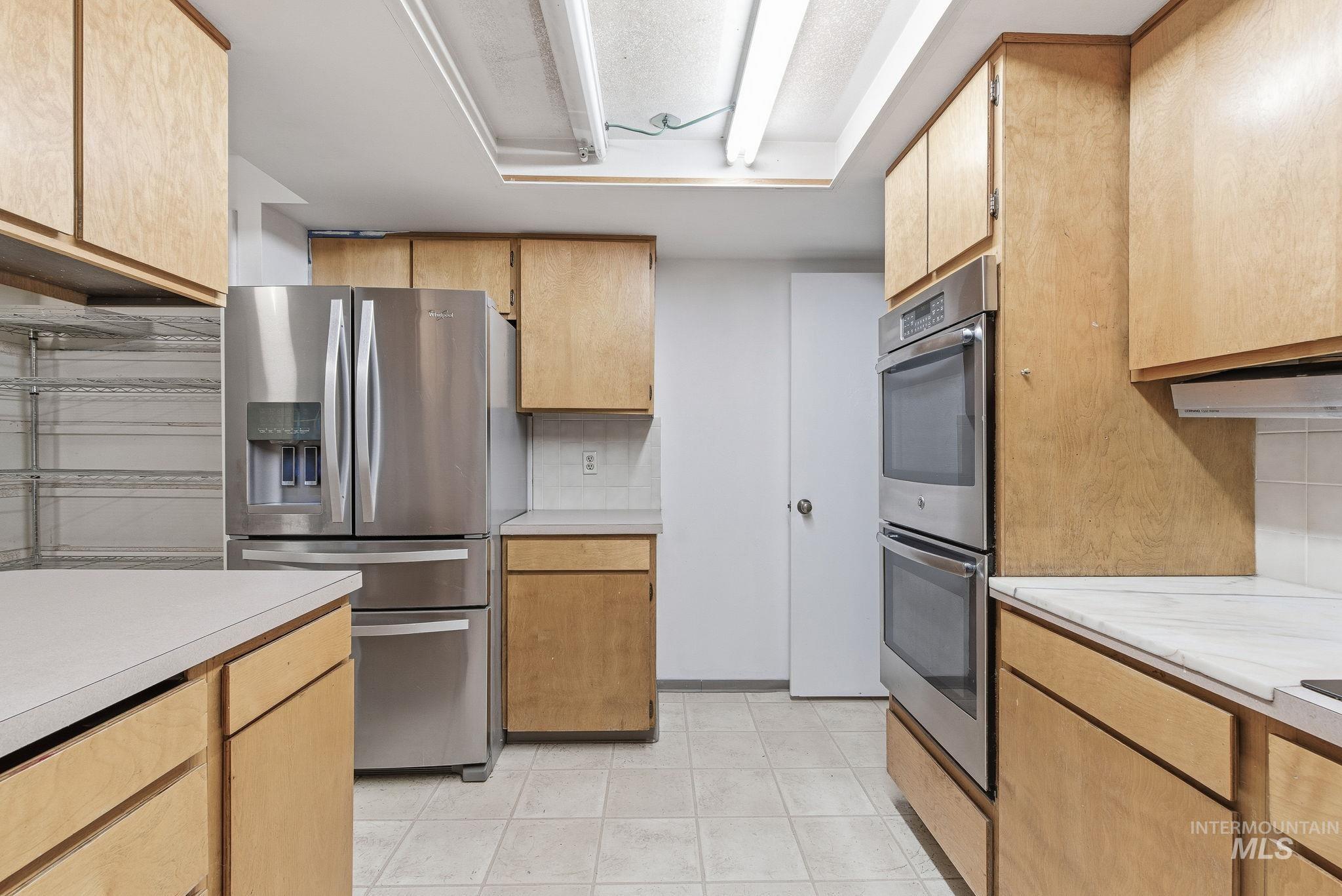 Kitchen with appliances with stainless steel finishes, light countertops, light tile patterned floors, and tasteful backsplash