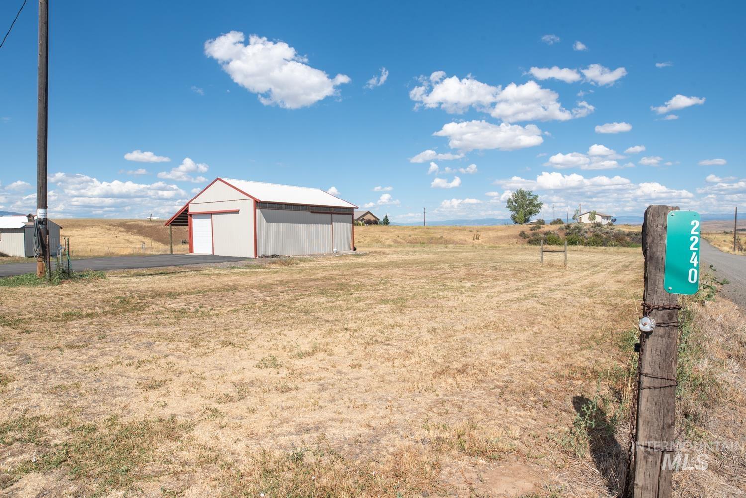View of green lawn with a garage, an outbuilding, a pole building, and asphalt driveway
