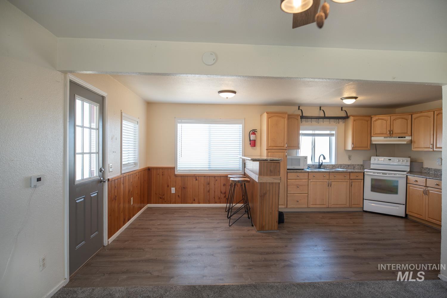 Kitchen with light brown cabinets, white appliances, dark wood-style floors, a wainscoted wall, and a breakfast bar area