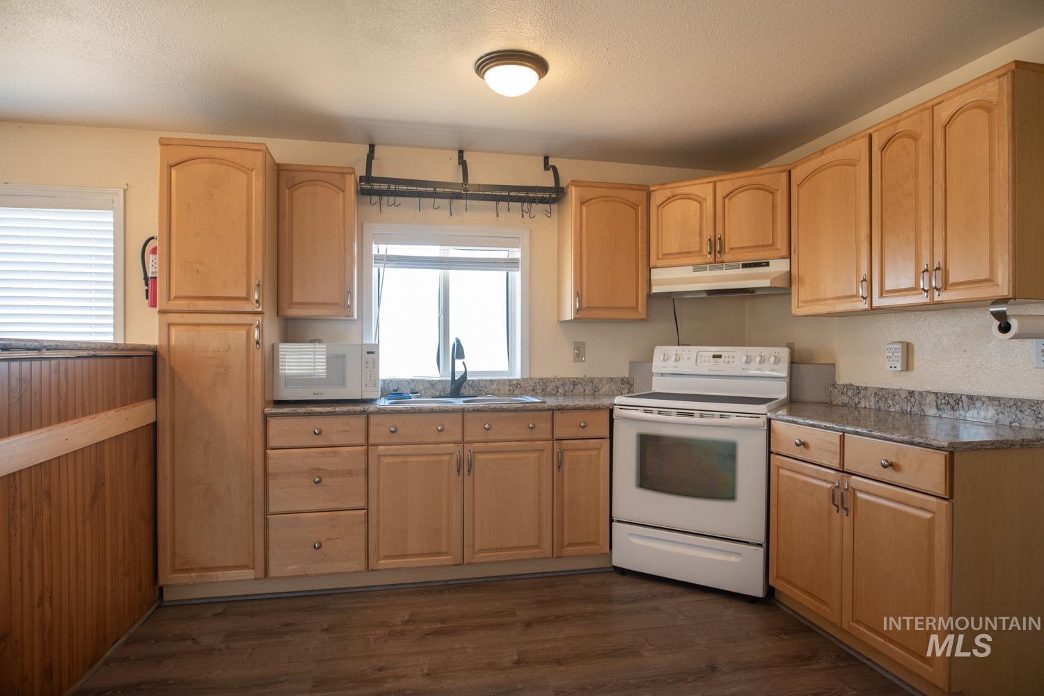 Kitchen with white appliances, light brown cabinetry, and under cabinet range hood