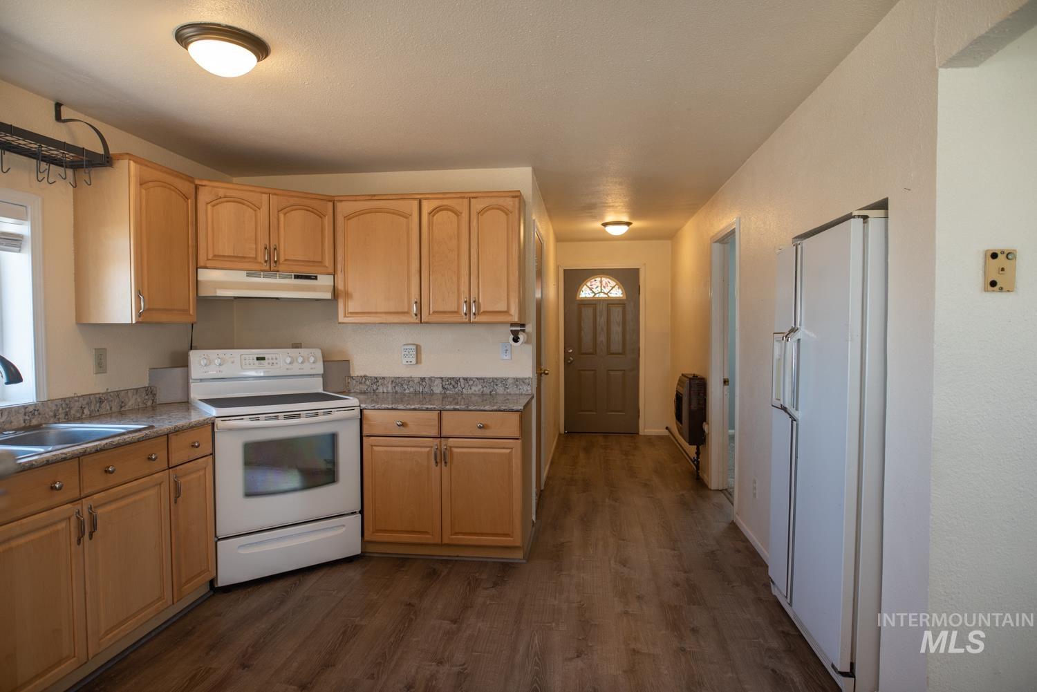 Kitchen with white appliances, dark wood finished floors, under cabinet range hood, and light brown cabinets