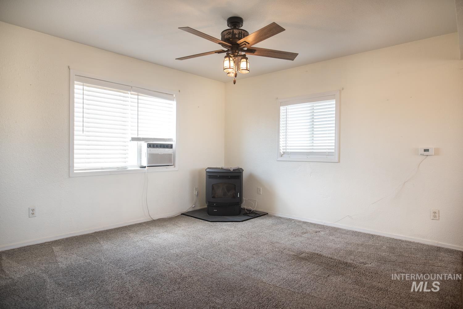 Empty room featuring a wood stove, a ceiling fan, carpet floors, and cooling unit