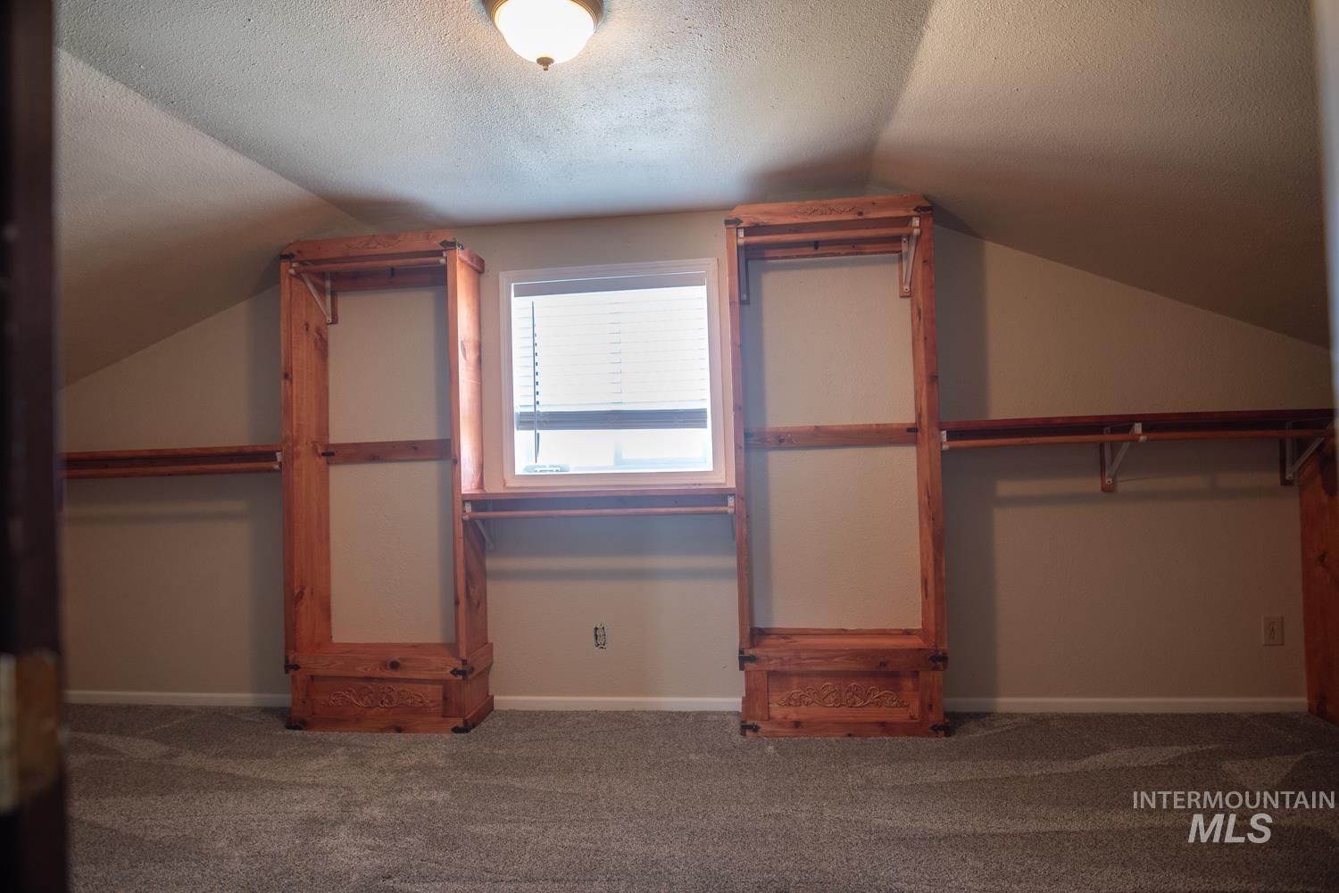 Unfurnished bedroom with vaulted ceiling, carpet flooring, and a textured ceiling
