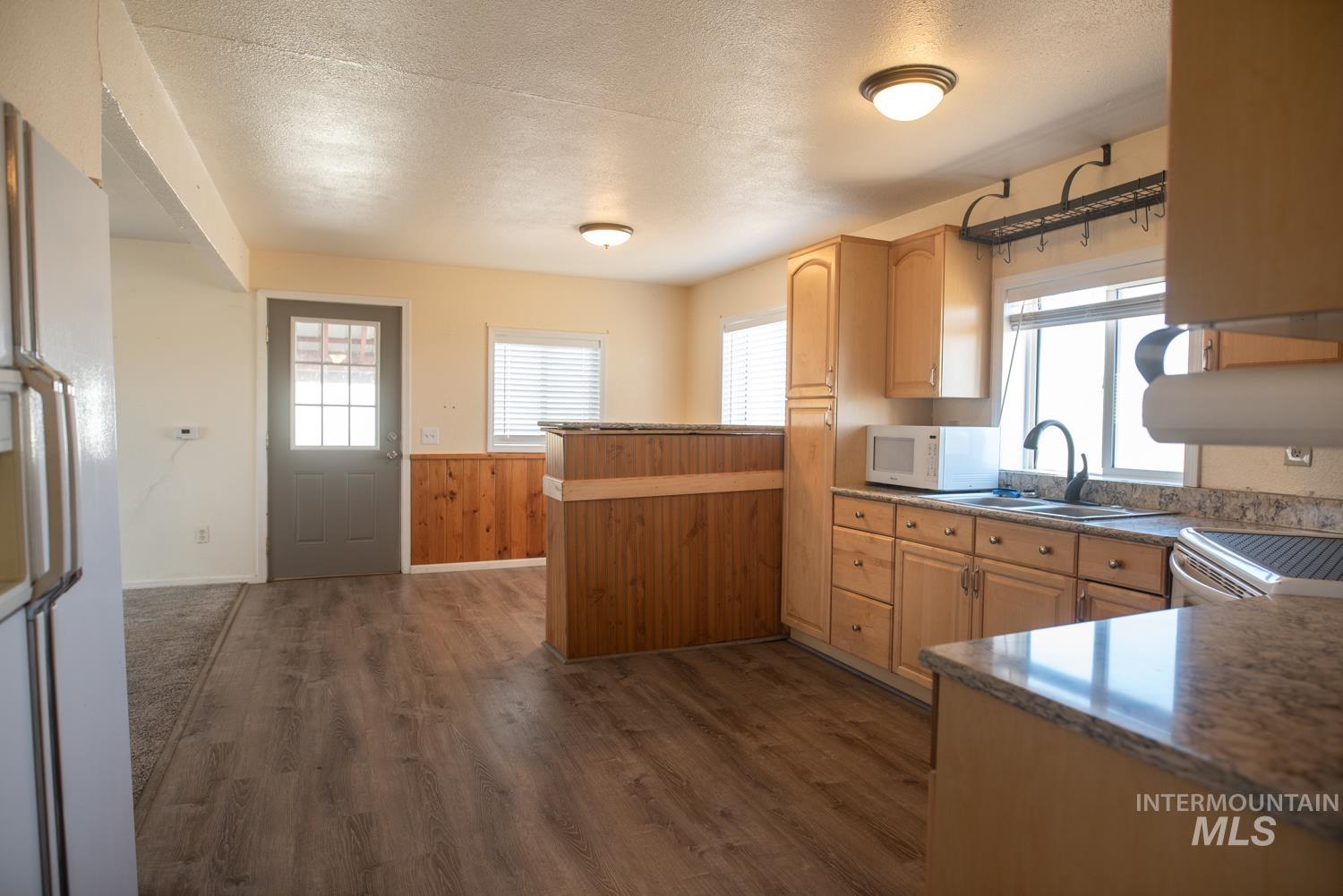 Kitchen with a peninsula, dark wood-style floors, white appliances, a textured ceiling, and a wainscoted wall