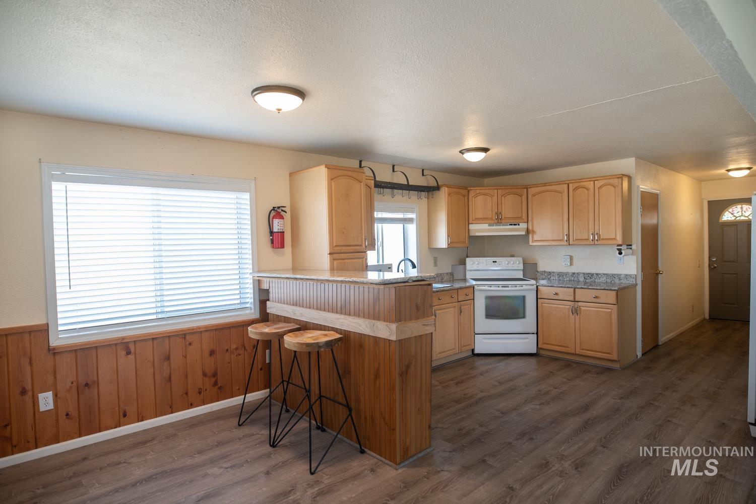 Kitchen with light brown cabinets, a kitchen breakfast bar, white electric range oven, dark wood finished floors, and a wainscoted wall