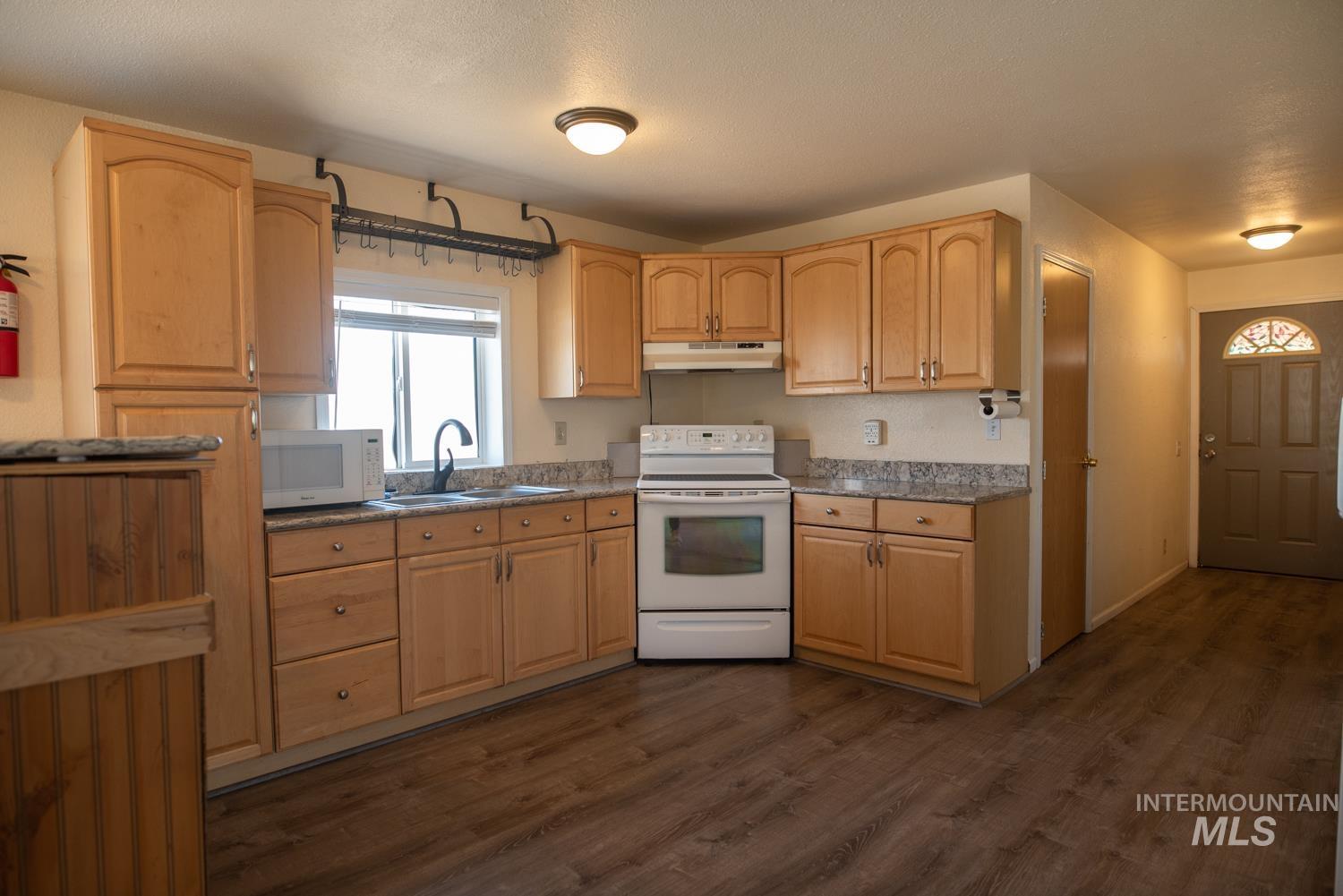 Kitchen with white appliances, light brown cabinets, dark wood-type flooring, and under cabinet range hood