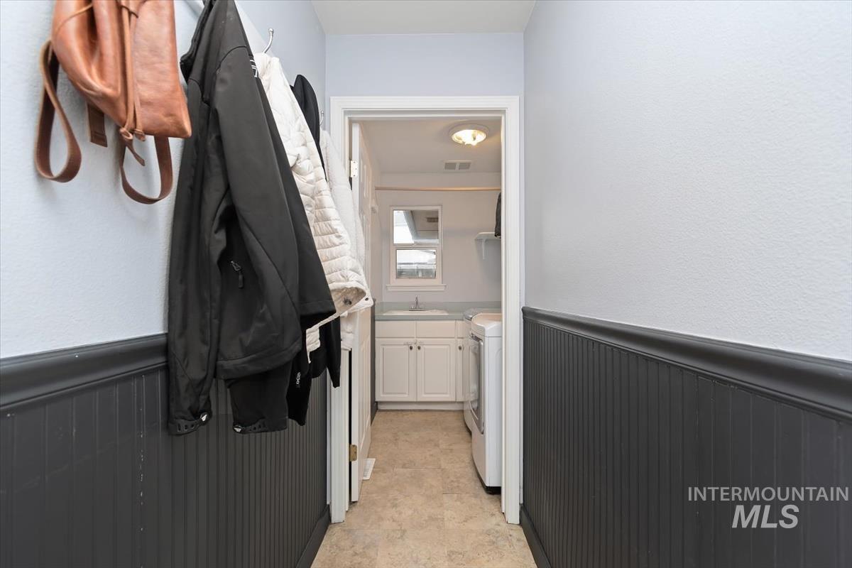 Hallway featuring dark beadboard wainscoting and light-toned walls, leading to a utility space with a white vanity and window
