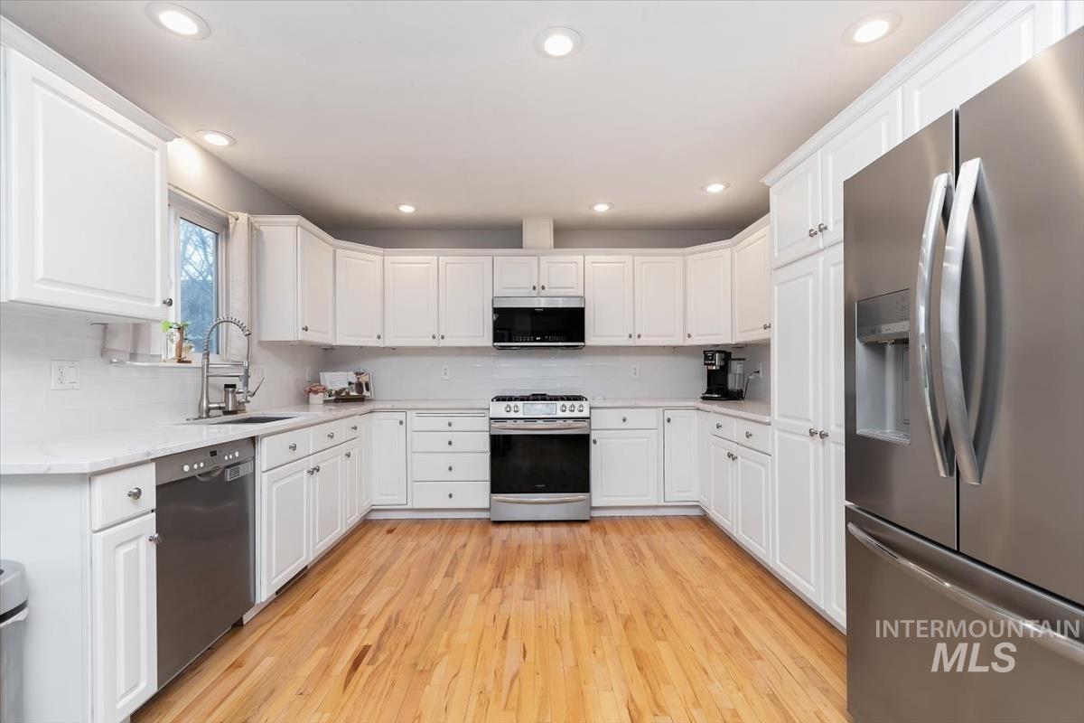 U-shaped kitchen featuring white shaker cabinetry, stainless steel appliances, light-toned wood-finish flooring, recessed lighting, and a window above the sink
