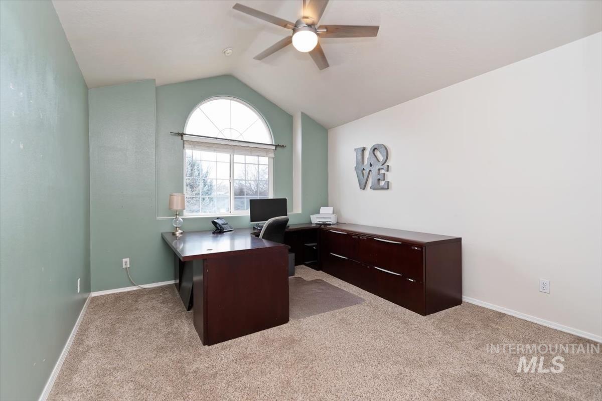 Carpeted room featuring a large arched window, vaulted ceiling, and ceiling fan with integrated lighting