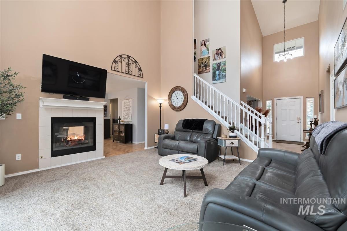 Vaulted ceiling living room featuring a tiled fireplace with mantel, carpet flooring, a white staircase with balusters, and a front entry door with sidelights