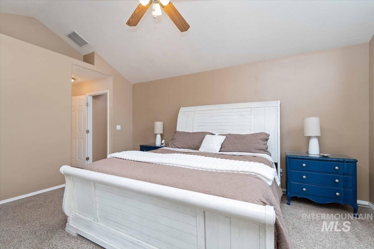Carpeted room featuring a vaulted ceiling with a ceiling fan, neutral wall paint, and a white interior door