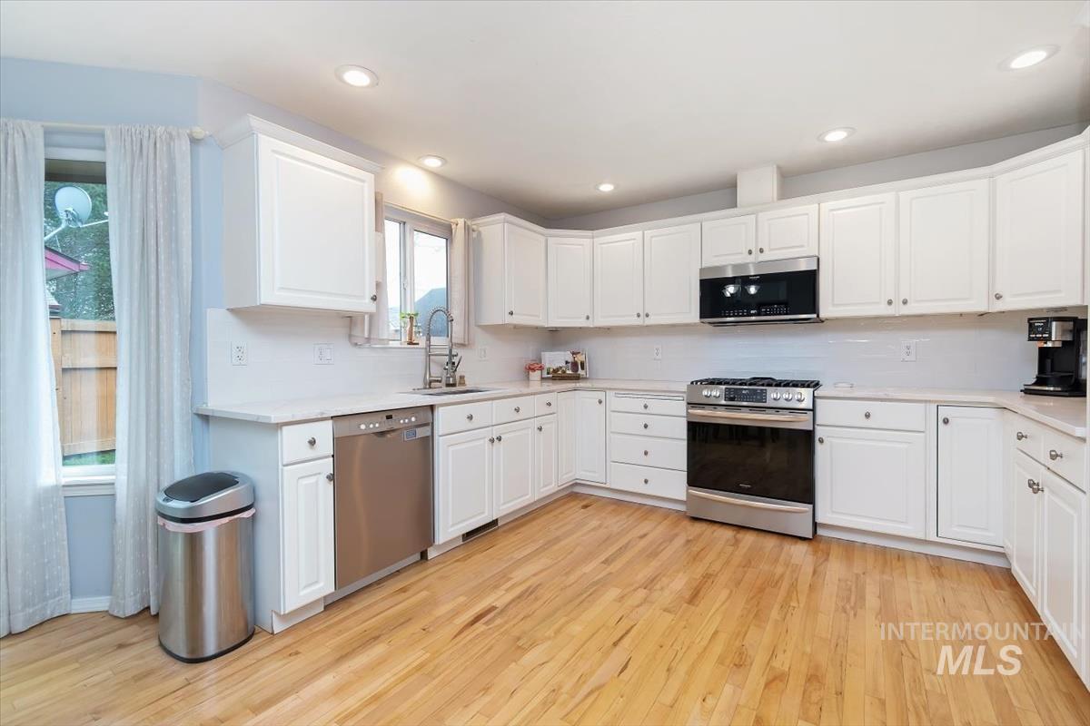 Expansive kitchen featuring wood-finish flooring, white cabinetry, integrated stainless steel appliances, recessed lighting, and a white tile backsplash