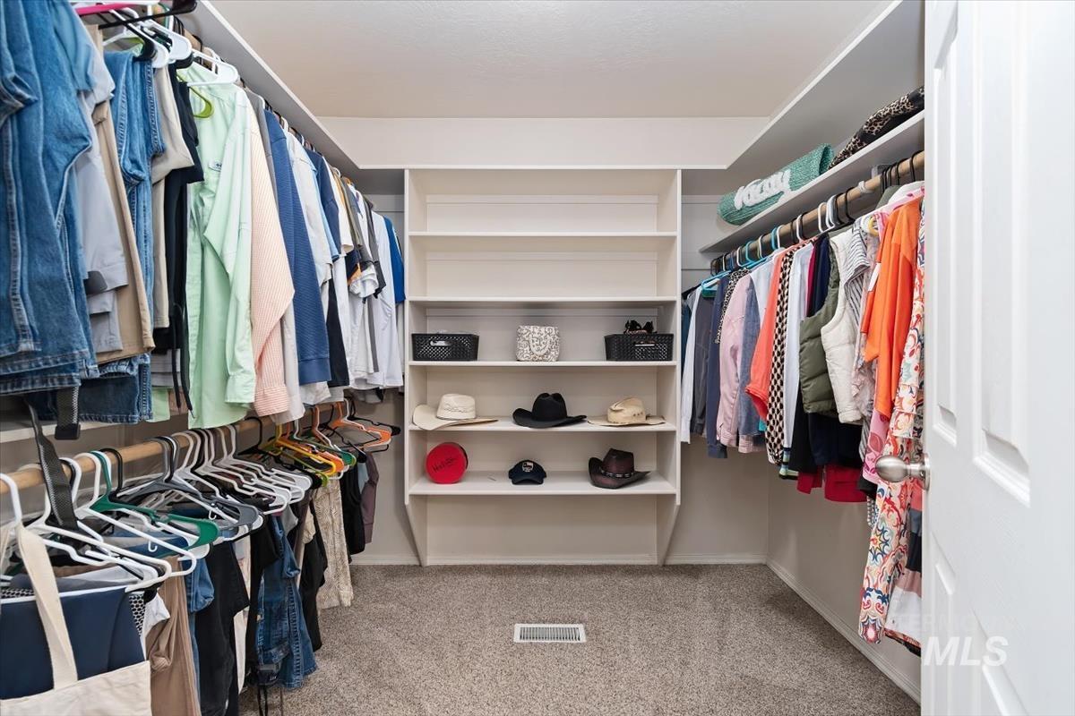 Walk-in closet featuring extensive built-in shelving, multiple hanging rods, and neutral-toned carpeting in the Master Suite