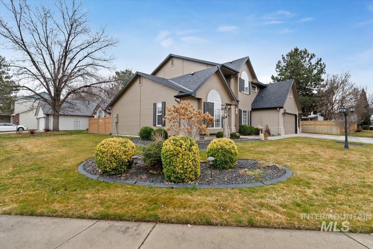 Traditional-style residence featuring a tan exterior, dark shingles, an arched window, and a two-car garage