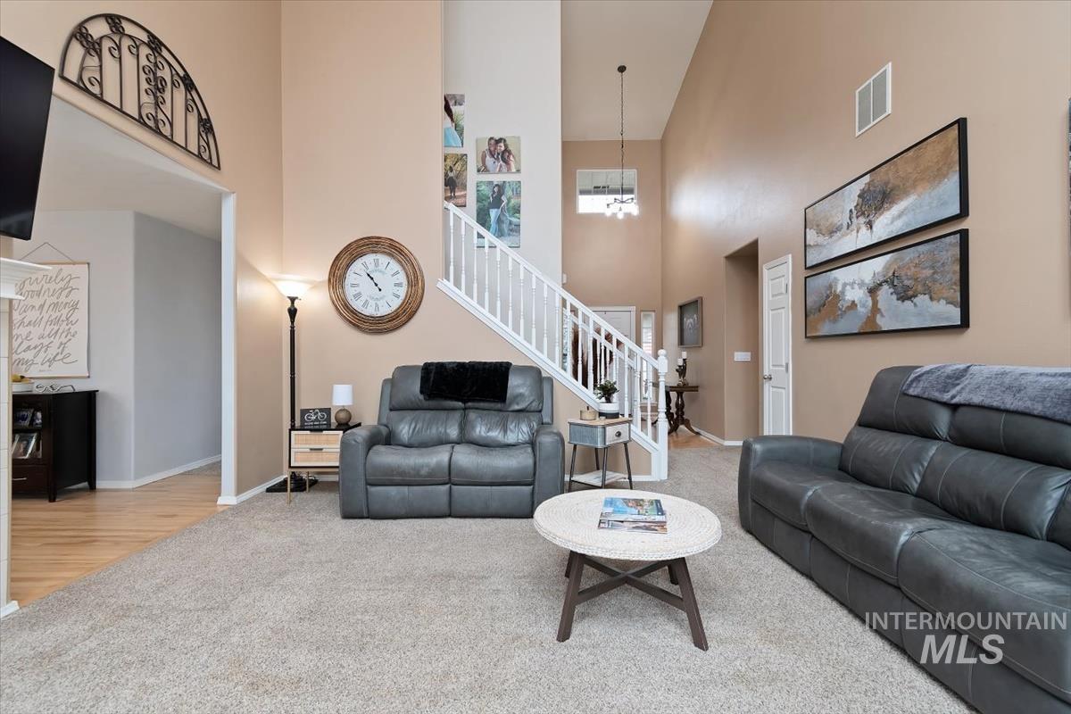 Vaulted ceiling living area featuring neutral carpeting, a staircase with white balusters, and a decorative arched wall accent