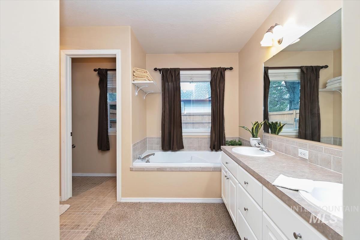 Master Bathroom featuring a built-in tub with tile surround, a dual-sink vanity with white cabinetry, a large wall-mounted mirror, and overhead lighting