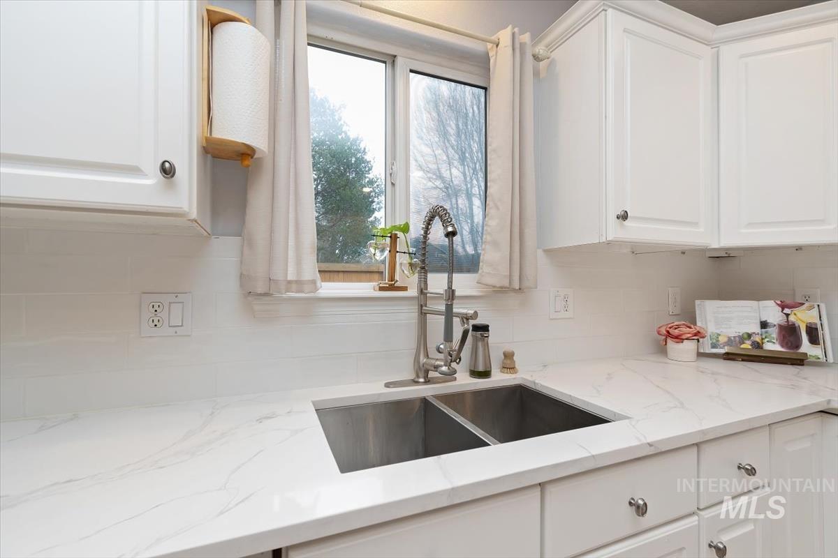 Kitchen featuring white shaker-style cabinetry, a dual-basin stainless steel sink with a pull-down faucet, and light-toned countertops with subtle veining