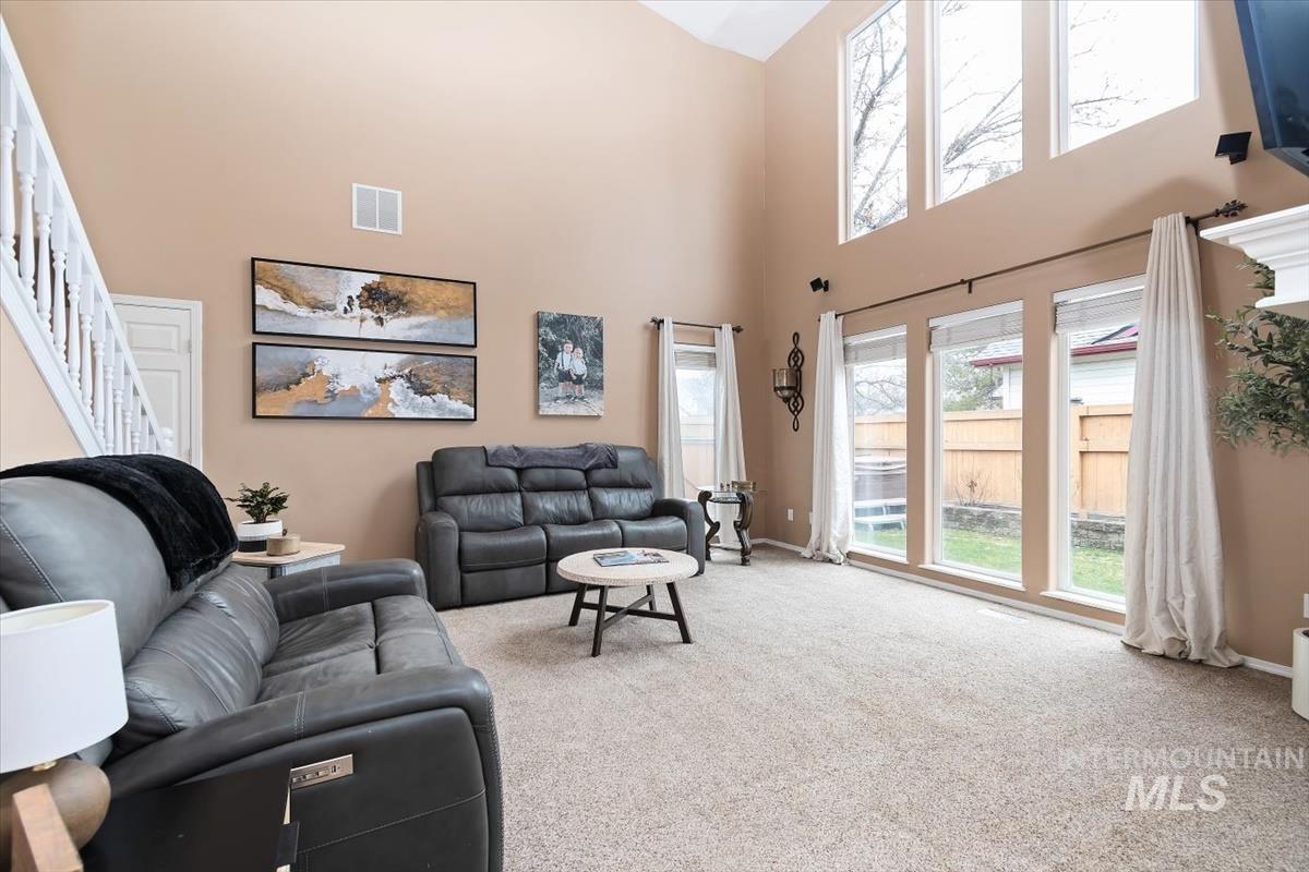 Two-story living area featuring a vaulted ceiling with upper windows, multiple large windows providing abundant light, and a white staircase with balusters