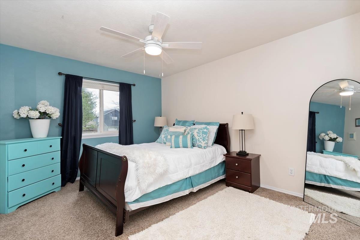 Carpeted room featuring a ceiling fan with integrated lighting, a window with dark drapery, and a rich wood-finish bed frame