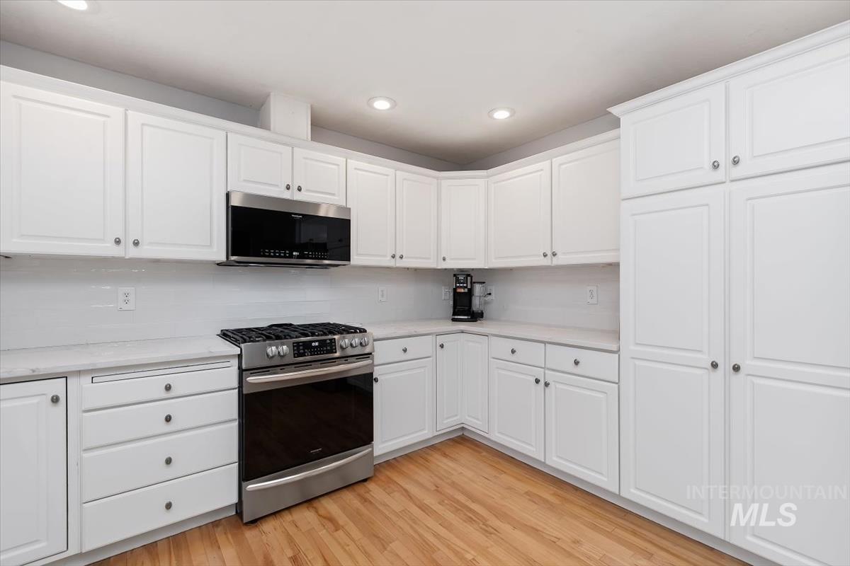 Kitchen featuring white shaker-style cabinetry, light-toned countertops, a full suite of stainless steel appliances, white subway tile backsplash, and wood-finish flooring