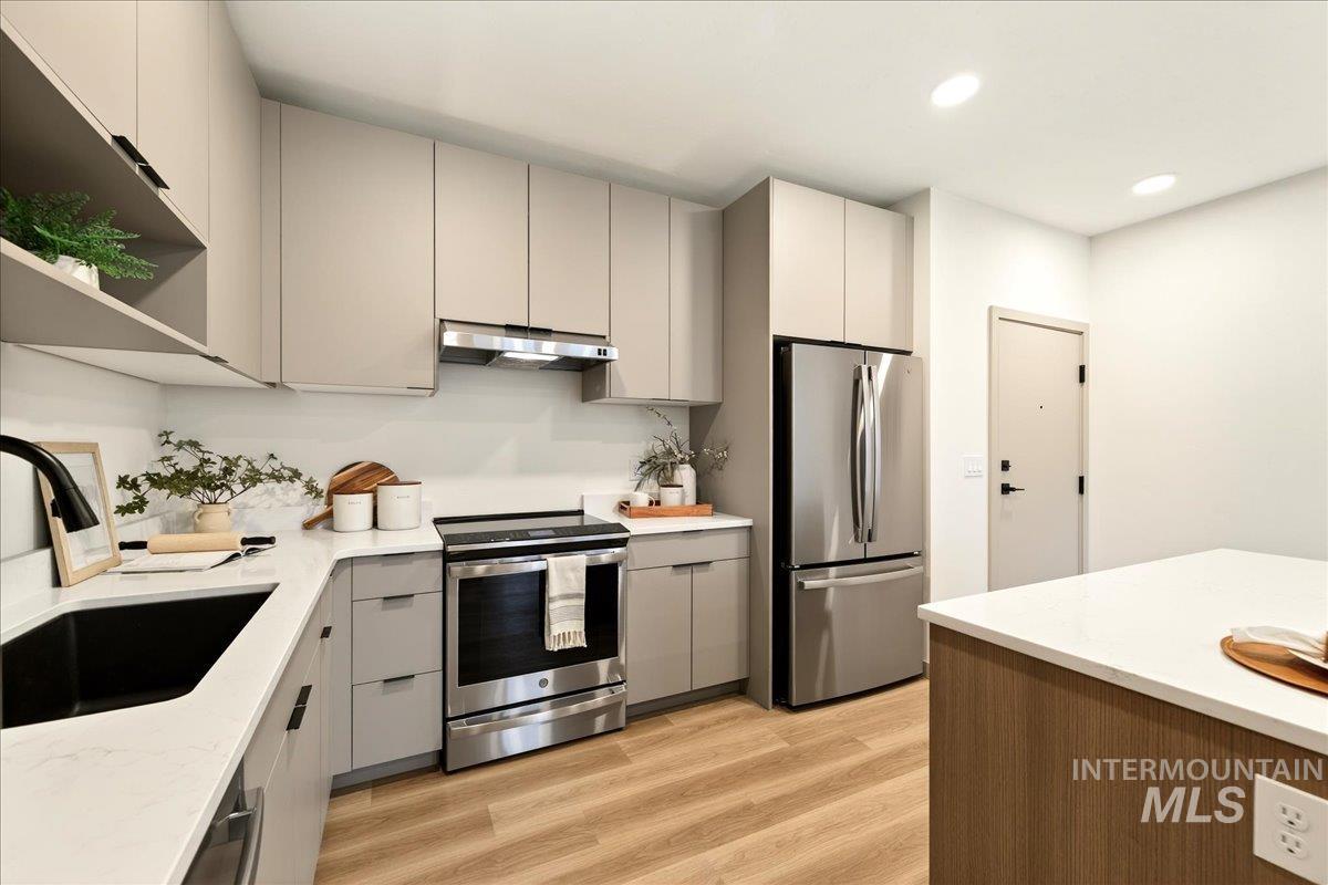 Kitchen with open shelves, gray cabinets, stainless steel appliances, light wood-type flooring, and light stone countertops